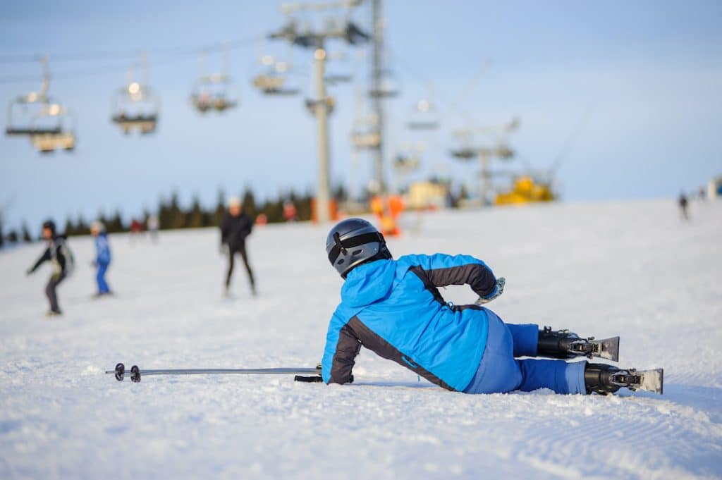 Young woman skier in blue ski suit after the fall on mountain slope trying get up
